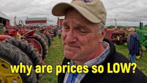 En man med bekymrad blick framför rader av traktorer på en auktion.